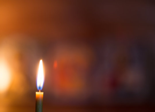 A burning candle against the background of orthodox icons in a dark room