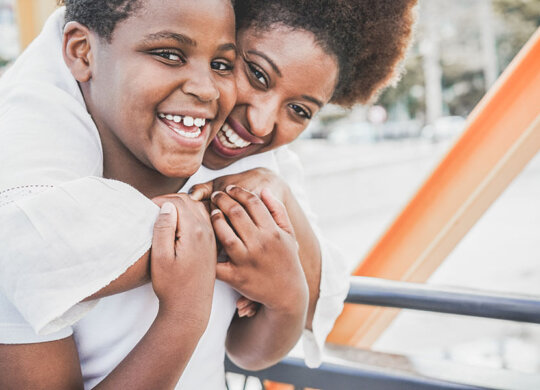 Happy african mother having fun with her child in summer day - Son kissing his mum outdoor during vacation day - Family lifestyle, motherhood, love and tender moments concept - Focus on kid face